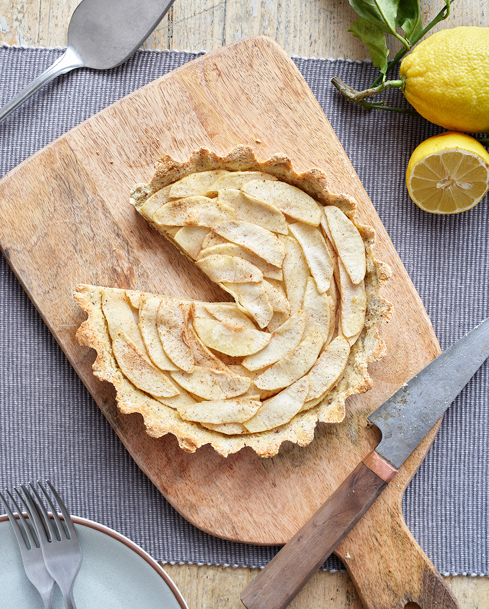 A photo of an apple tart with sliced apples on top. One slice is missing.