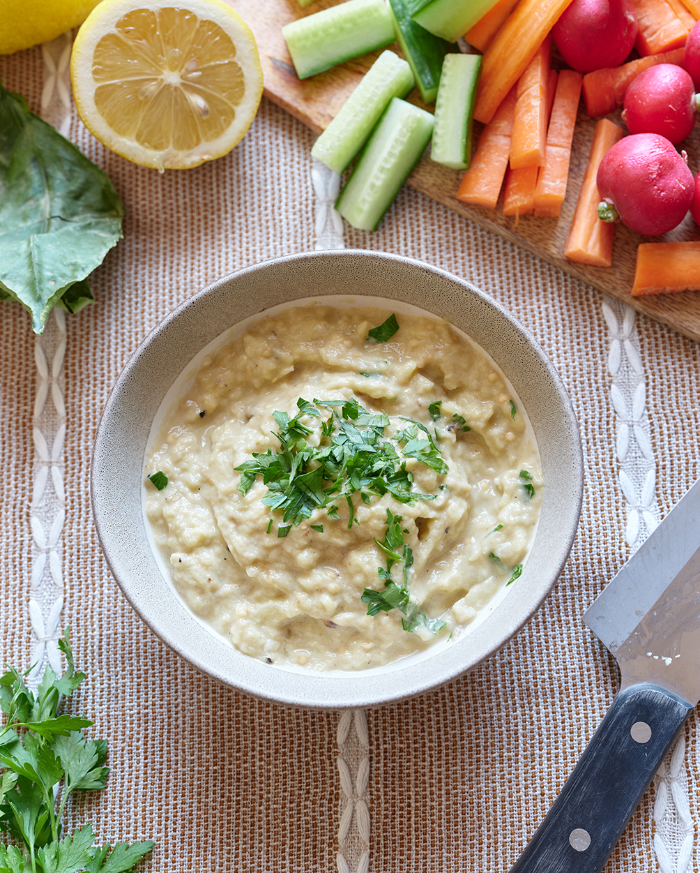 A bowl of Baba Ghanoush with a herb garnish and vegetable crudities