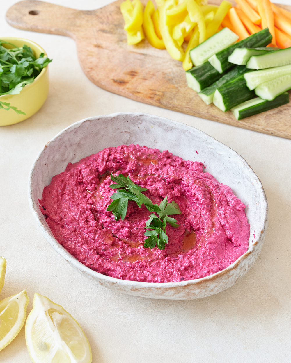 A bowl of pink beetroot hummus with vegetable crudities in the background