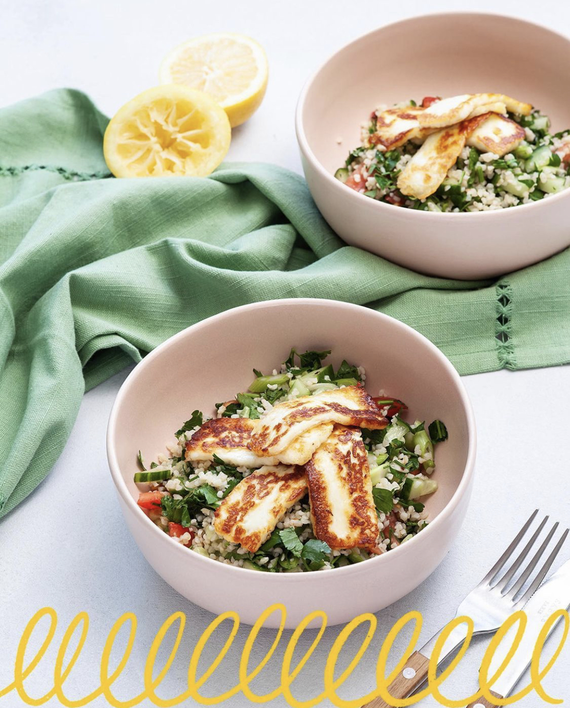 Two bowls of quinoa and vegetable salad topped with slices of halloumi